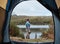 Man by lake from tent view, outdoor and camping for adventure, vacation or holiday in nature. Explorer, binocular and