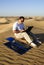 Man with a laptop and a portable folding solar kit charger in the midst of desert sand dunes