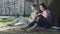 Man with laptop sitting under tree and looking at girl reading book, affection