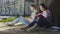 Man with laptop sitting under tree near girl reading book, contemporary youth