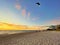 Man launching kiteboard sail on beach at sunrise.