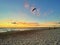 Man launching kiteboard sail on beach at sunrise.