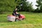 Man lawn mower drives through large green meadow garden