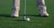 Man legs swinging golf putter club on course field. Player feet stand on grass.
