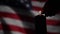 A man lights a candle against the background of the waving flag of the United States of America in the dark.