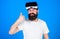 Man with long beard and serious face showing OK gesture. Hipster with trendy beard wearing VR goggles, digital