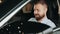 Man looking at a car in a car showroom. Portrait happy smiling young man buyer sitting in his new car excited ready for