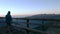 Man looking at mountain view at sunrise from wooden balcony and drinking hot beverage from mug, high up on the Alps