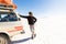 Man looking at sun, SUV driving Salar De Uyuni desert.