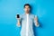 Man looking surprised, showing smartphone screen and glass of water, standing over blue background