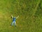 Man lying on the ground in a park on a green grass field. Man dressed in blue t shirt and jeans Hands apart black base ball hat on