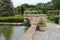 A man made stone waterfall flowing into a large koi pond with stone pavers leading to a landscaped garden