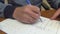 A man makes corrections in entries on a sheet of white paper with a ballpoint pen in blue ink, close-up