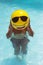 Man is making fun in the pool, having inflatable yellow ball infront of his face