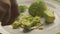 A man is mashing avocado into puree on a white plate with a fork in close-up.