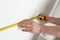 Man measuring white wall indoors, closeup.