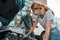 Man in medical mask helping girl with her auto while she is examining, looking at her broken car with open hood