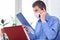 A man with a medical mask on his face reads a document in the office and talks on the phone