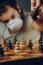 A man in a medical mask moves a token on a chess board full of pawns