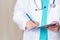 A man in a medical robe takes notes. Close-up, cropped doctor with stethoscope and tablet for records.