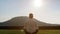 Man meditates on grass on sunny day against big green hill