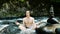 Man meditates in the lotus position in a cold mountain river among the stones and a cairn