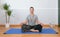 Man meditating on the lotus position inside his house on a mat with a Buddhist necklace mala