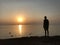A man meets the dawn on the seashore. A man watches the morning sun over the ocean. Sunset on the coast, a sunny circle over the