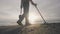 Man with metal detector searches treasures on the ocean tropical sand beach among the ruins with his dog at sunrise.