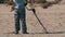 Man with a Metal Detector Walks along a Sandy Beach on the Seashore