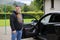 Man of middle age, with long beard stands questioningly before an open car door