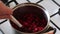 A man mixes sugar and frozen cranberries in a saucepan. Stirs with a spoon. Prepares mashed potatoes for marshmallow.