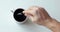 Man is mixing black coffee in cup with spoon on white table, hand closeup.