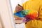 Man mixing paints on palette with brush near canvas in studio, closeup