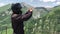 Man mototurist in motorcycle helmet standing on point view in the middle of green causacus mountains and making pictures