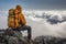 Man in mountaineering clothes with backpack sitting on a rock above the clouds and enjoying the view. Generative AI
