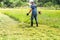 A man mows the grass with a trimmer on a sunny day. Back shot of a farmer mowing grass in the backyard. A quiet scene. A view from