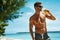 Man With Muscular Body Drinking Healthy Drink On Beach. Summer