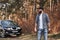 Man and nature. Bearded man near his brand new black car in the forest. Vacations concept