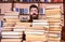 Man, nerd on surprised face between piles of books in library, bookshelves on background. Nerd concept. Teacher or