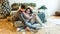A man in a New Year`s patterned sweater gently hugs his pregnant wife in the bedroom decorated for the New Year sitting on the