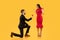 Man Offering Girlfriend Engagement Ring Standing On Knee, Yellow Background