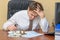 The man at the office, holding his head looking at the notice of the accident with the money and the machine lying on the document