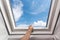 Man open new skylight mansard window in an attic room against blue sky.