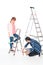 man opening paint tin and girlfriend standing near on ladder with paint roller