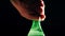 Man opens green plastic bottle of foamy soda against black background