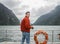 Man in orange down jacket with camera on passenger cruise for taking photos at Milford Sound in New Zealand
