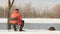 A man in an orange jacket catches fish in the winter. On the shore of an icy river. Shore in the snow