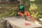 A man in an orange jacket cuts boards with an alaskan mobile chainsaw mill at sunny day.