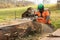 A man in an orange jacket on the side of a field cuts boards with an alaskan mobile chainsaw mill